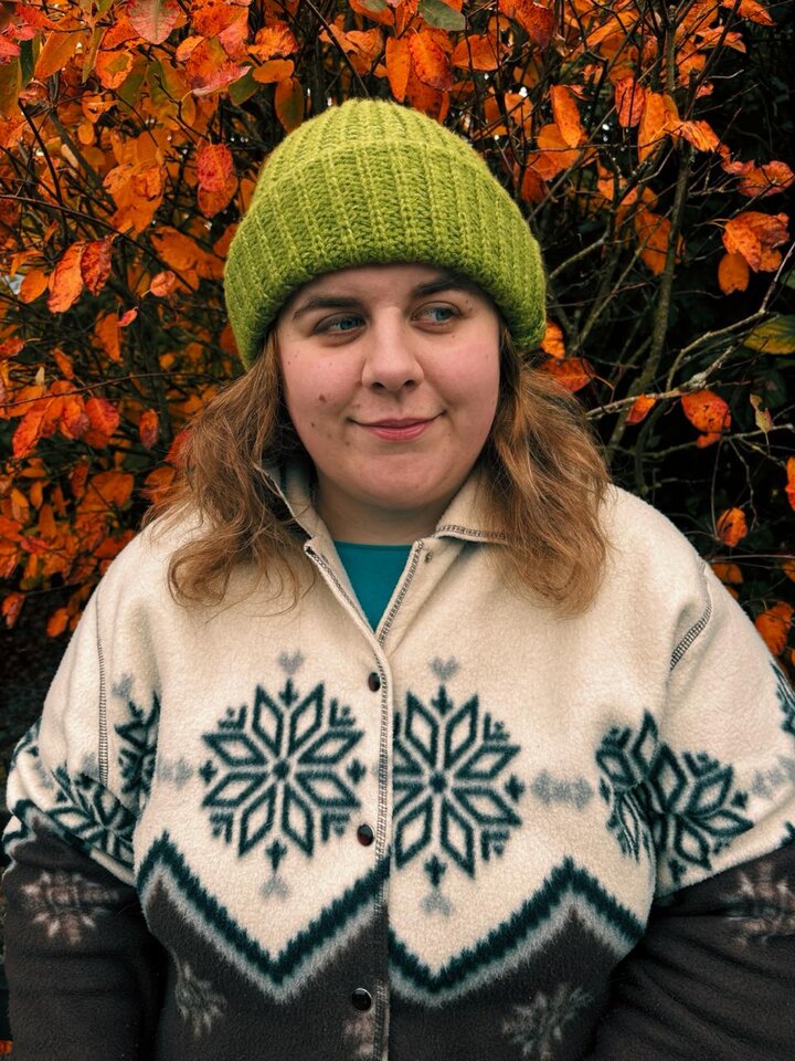 Miśka, wearing a green beanie, in front of autumn foliage